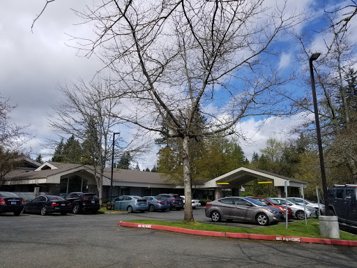 A view of a building with a parking lot surrounded by trees under a partly cloudy sky.