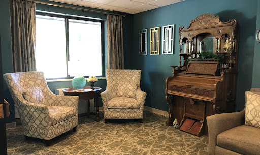 A cozy living room featuring patterned chairs, a vintage piano, and tasteful wall decorations.
