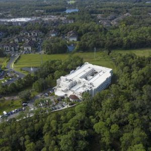 Aerial view of a large building surrounded by a forested area in a suburban landscape.