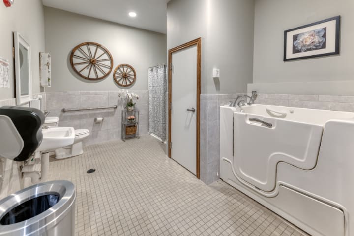 A spacious, accessible bathroom featuring a walk-in tub, toilet, and shower with grab bars for safety.