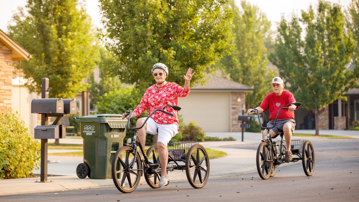 Elderly individuals enjoying a ride on tricycles through a neighborhood street.