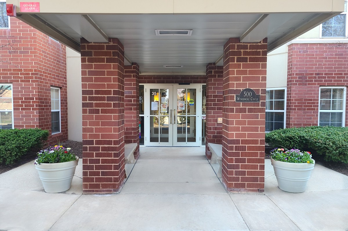 Entrance with brick columns and glass doors flanked by potted plants.