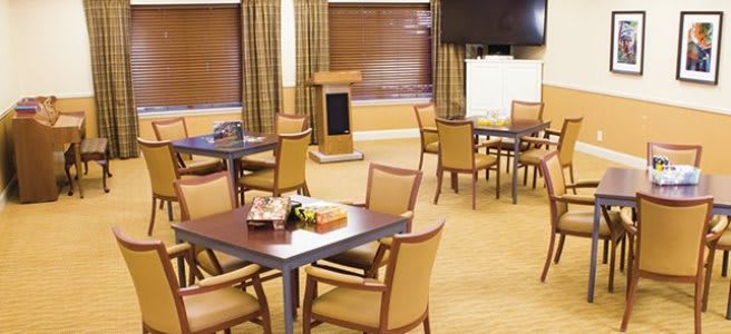 An empty conference room set up with tables and chairs, featuring a podium and television.