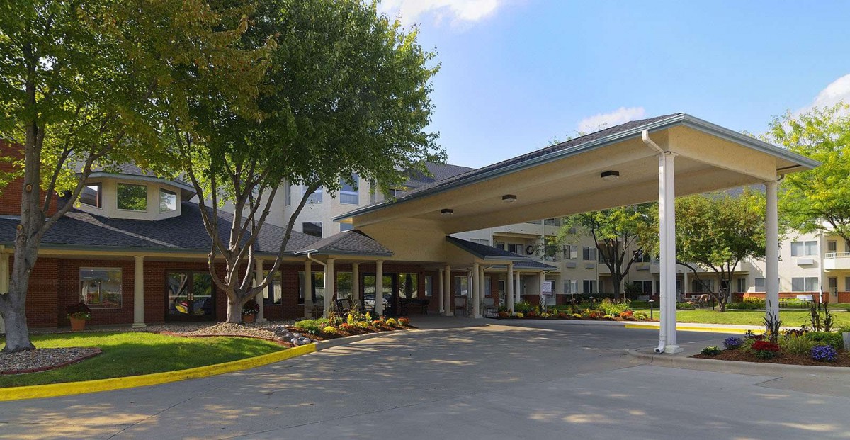 The entrance of a building with a covered driveway surrounded by trees on a clear day.