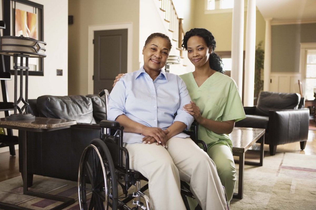 A caregiver smiling with an elderly person in a wheelchair.