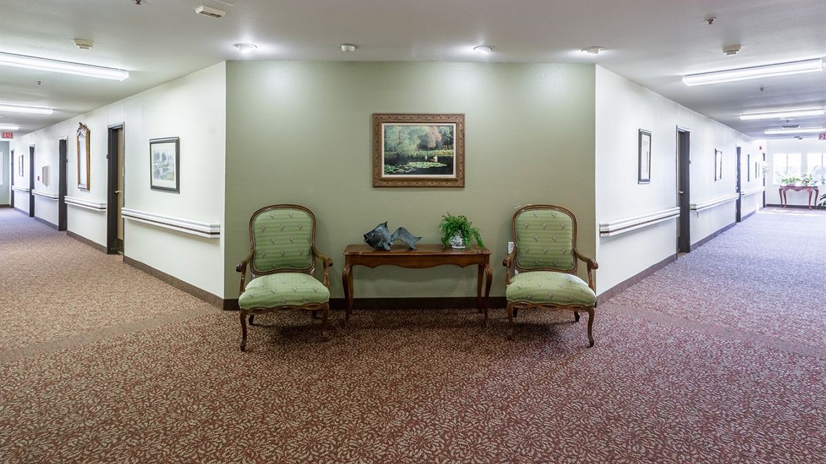 A hallway with two upholstered chairs, a table, decorative plants, and a framed artwork.