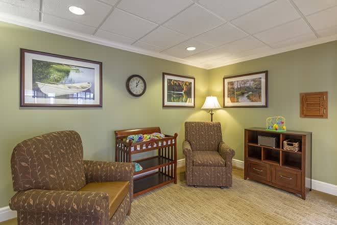 A cozy waiting room with chairs, decorative art on the walls, a clock, and a lamp. There's also a small toy area for children.