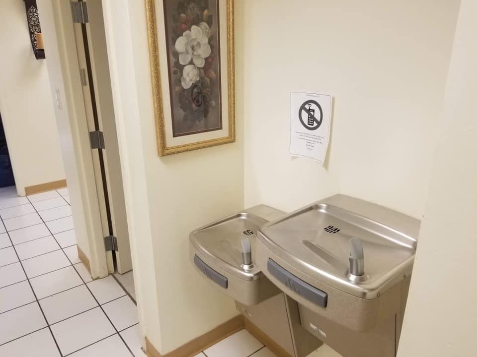 Two water fountains in a hallway with a framed artwork and a sign on the wall.