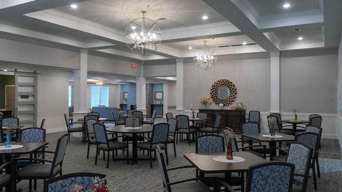 An elegantly decorated dining area featuring numerous tables and chairs, with chandeliers and a carpeted floor.