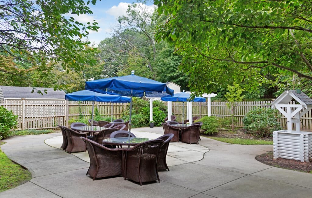 A tranquil outdoor patio with blue umbrellas and wicker furniture surrounded by greenery.