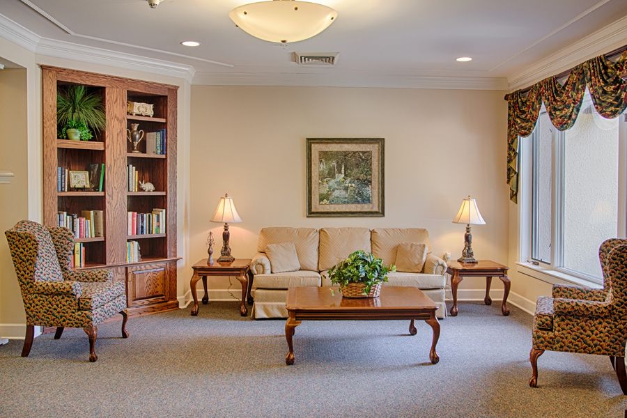 A cozy living room with a comfortable sofa, classic lamps, and a wooden coffee table, framed by bookshelves and artwork.