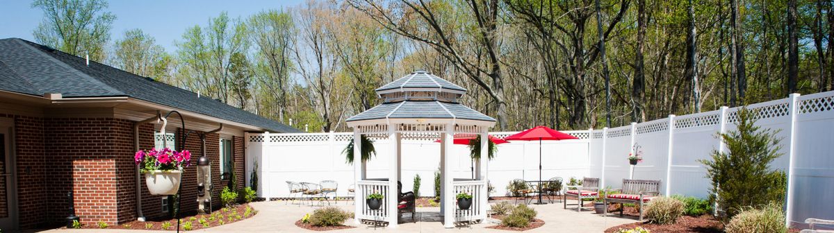 A charming white gazebo surrounded by nature, with trees in the background and hanging plants adorning it.