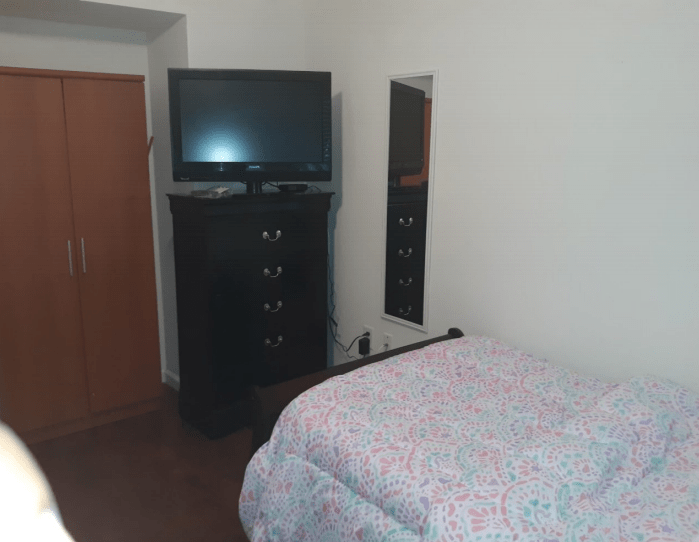 A simple bedroom with a bed, television, dresser, and mirror.