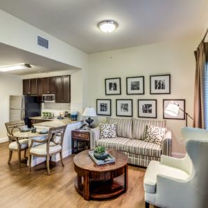 A cozy living room with an open kitchen, featuring a striped sofa, coffee table, and dining area.
