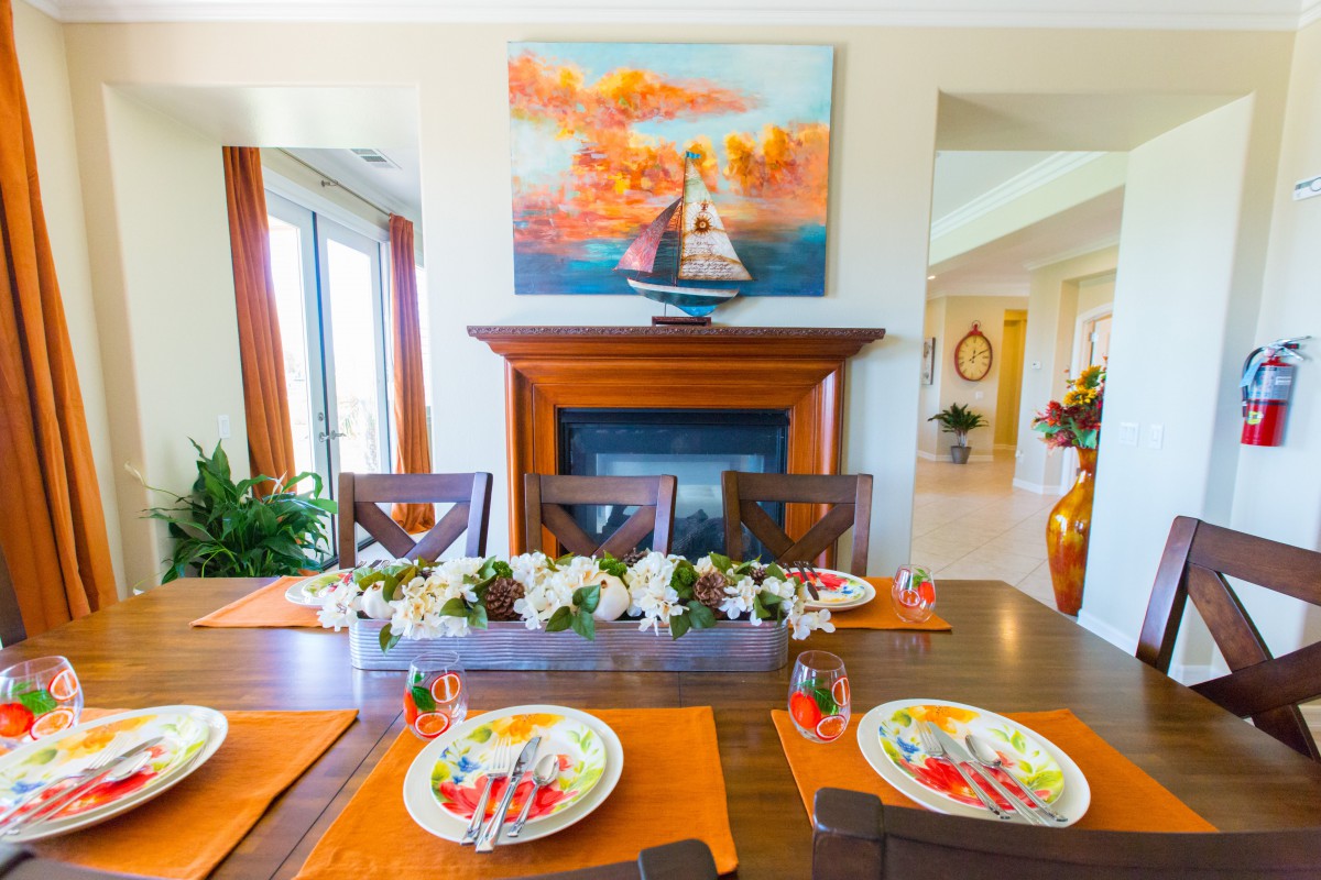 A vibrant dining room with an elegantly set table, featuring colorful plates and a centerpiece of flowers. A painting hangs above the fireplace, adding warmth to the room.