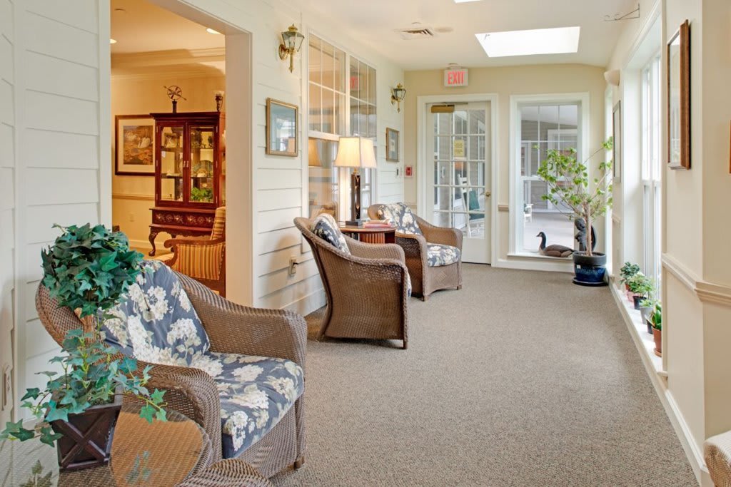 A cozy living area with wicker furniture, decorative plants, and ample natural light coming through glass doors.