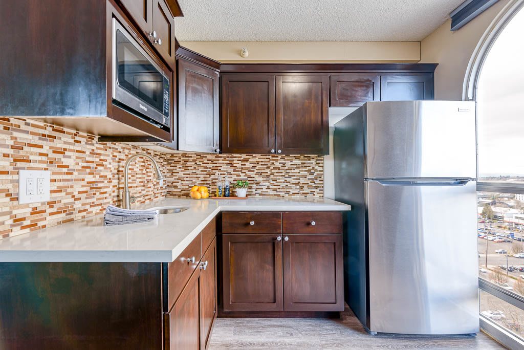 A modern kitchen featuring dark wooden cabinets, a stylish backsplash, and stainless steel appliances.