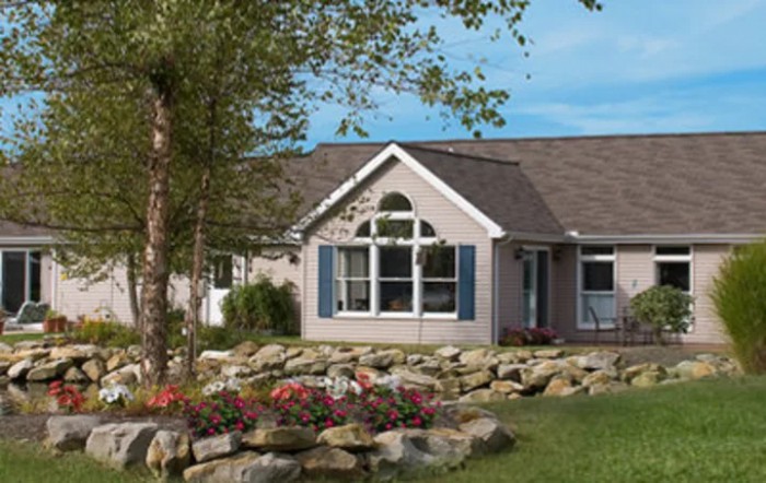 A single-story house with a well-maintained garden and blue shutters, surrounded by rocks and flowers.