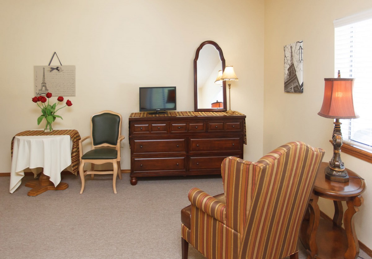 A cozy room with vintage furniture including a dresser, mirror, television, and striped armchair.