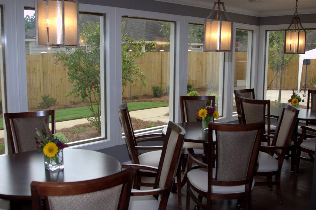 A cozy dining room with several tables and chairs, featuring large windows and modern lighting.