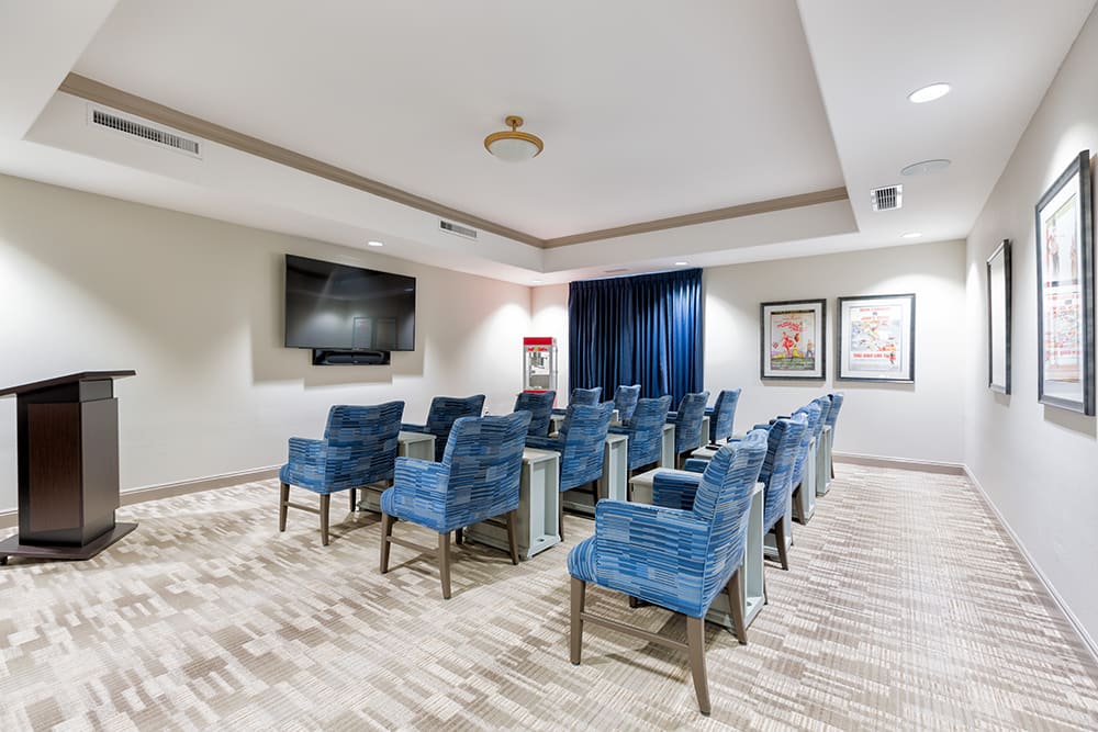 A small theater or conference room with blue upholstered chairs facing a large screen, surrounded by a modern interior design.