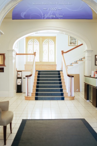 A bright and elegant hallway featuring a central staircase with a blue carpet.