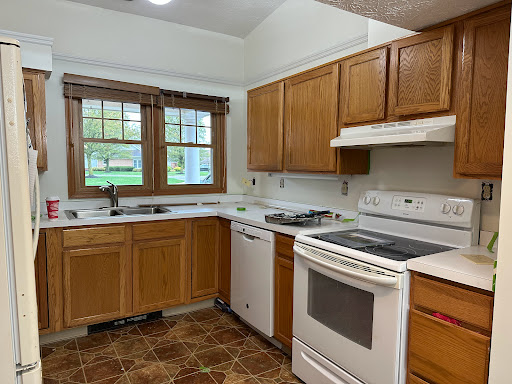 A cozy kitchen featuring wooden cabinets, essential appliances, and natural light from the windows.