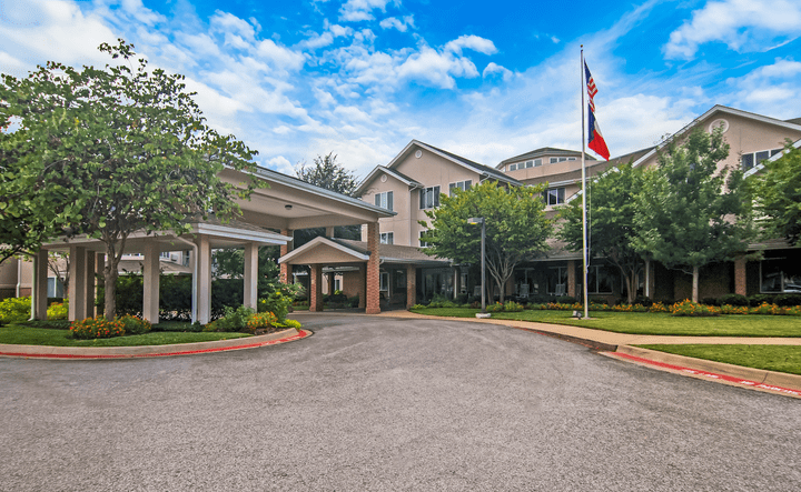 A large building with a driveway surrounded by trees and a flagpole under a cloudy sky.
