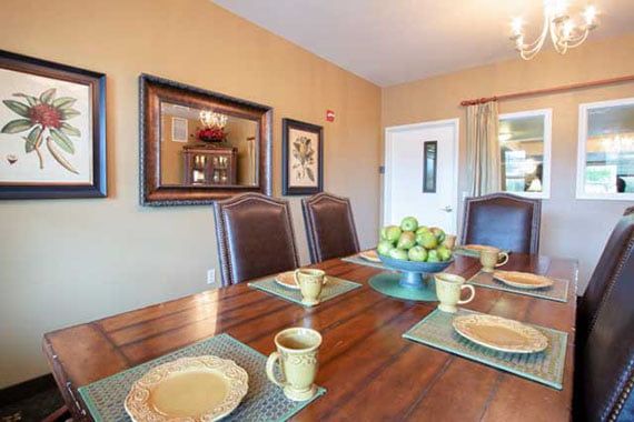A dining room setup with a wooden table adorned with place settings and a centerpiece of green apples.