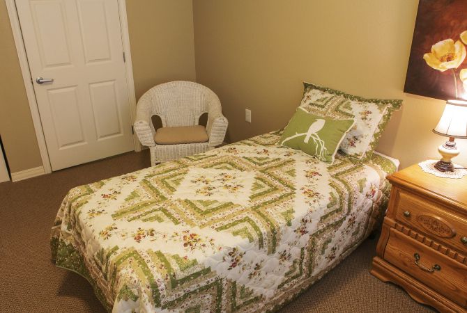 A cozy bedroom with a single bed featuring a patterned quilt and a decorative pillow, accompanied by a wicker chair.
