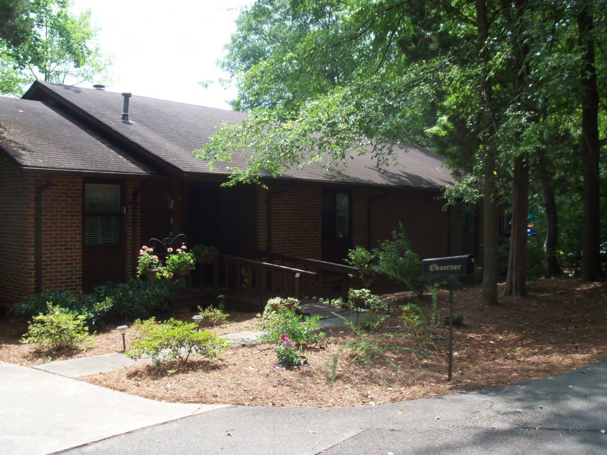 A wooden house surrounded by a garden with trees.