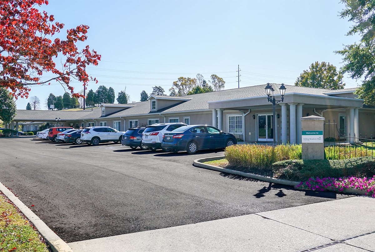 A sunny view of a parking lot in front of a motel with several parked cars and surrounding trees.