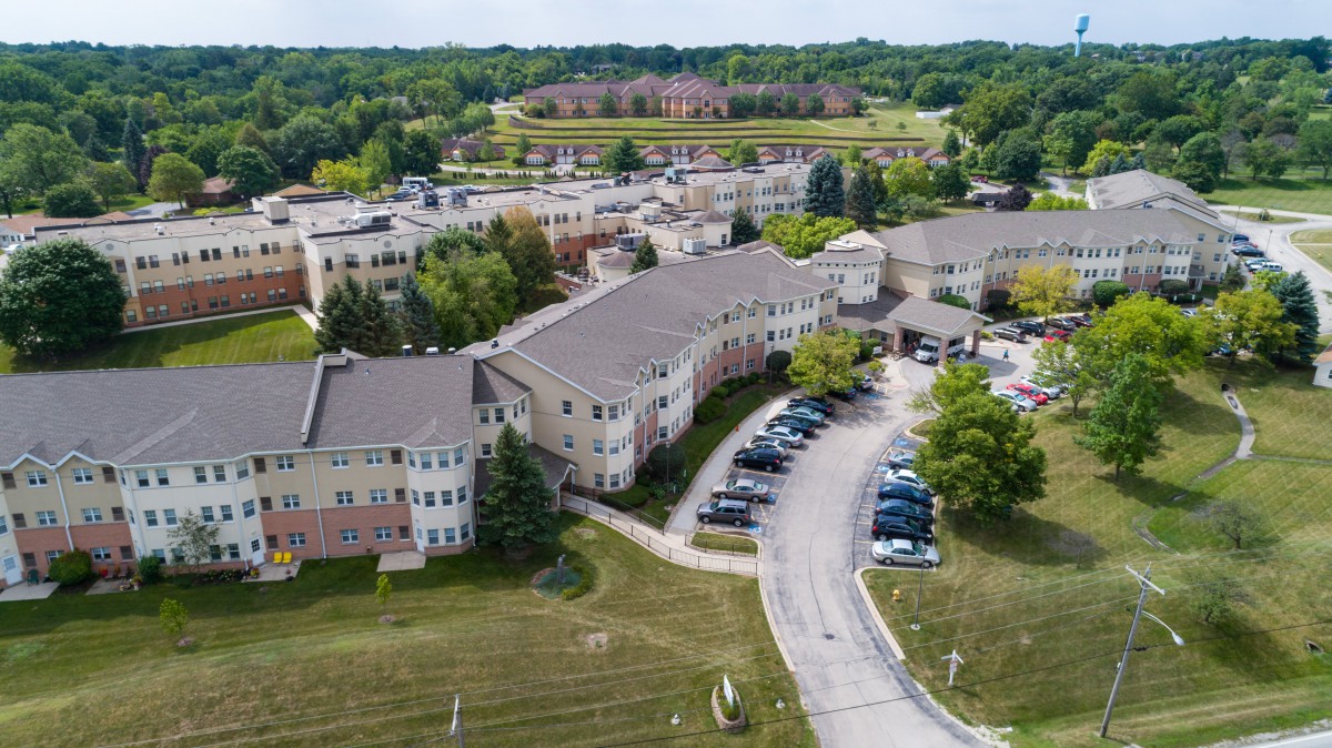 Aerial view of a complex with multiple buildings surrounded by greenery and a parking area.