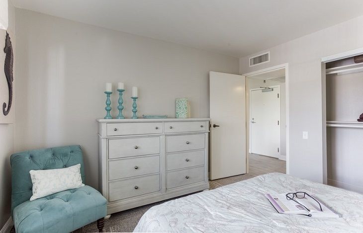 A cozy bedroom with a pastel color scheme featuring a dresser adorned with candles.