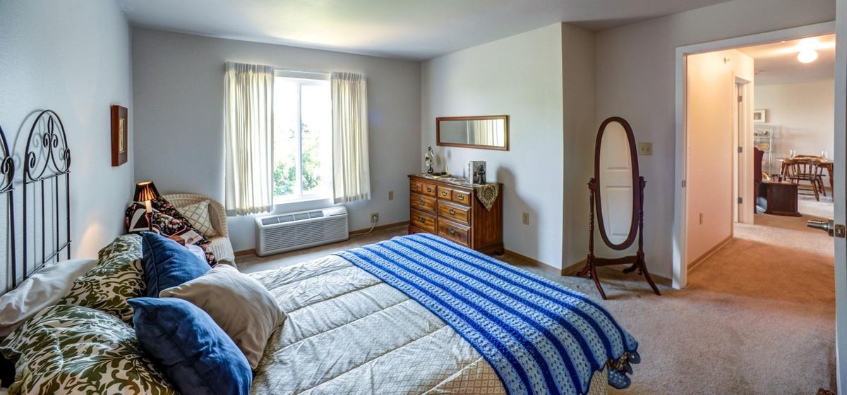 A cozy bedroom with a bed, dresser, and mirror, illuminated by natural light from the window.
