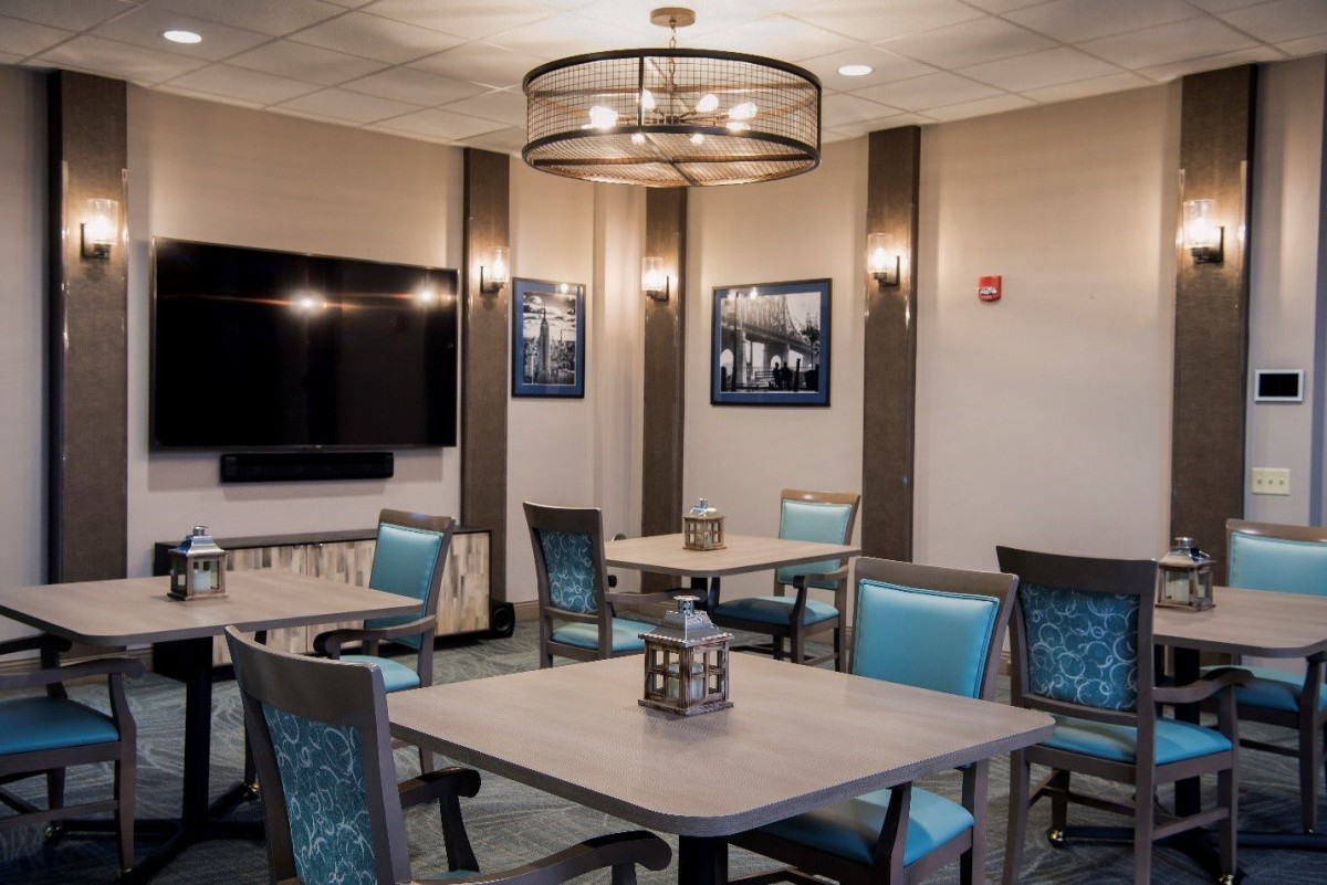 A modern meeting room with neatly arranged tables and chairs, featuring a large television and decorative lighting.