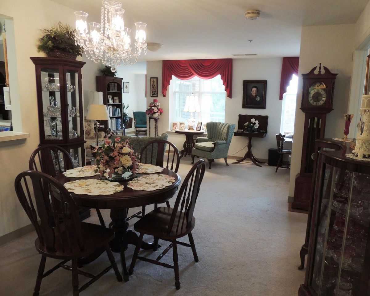 A cozy, traditionally decorated dining and living area featuring a chandelier, wooden furniture, and elegant curtains.