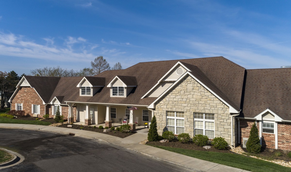 A spacious residential house with a stone facade and landscaped driveway under a clear blue sky.