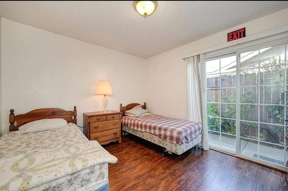 A simple bedroom with two beds, a nightstand, and a sliding glass door.