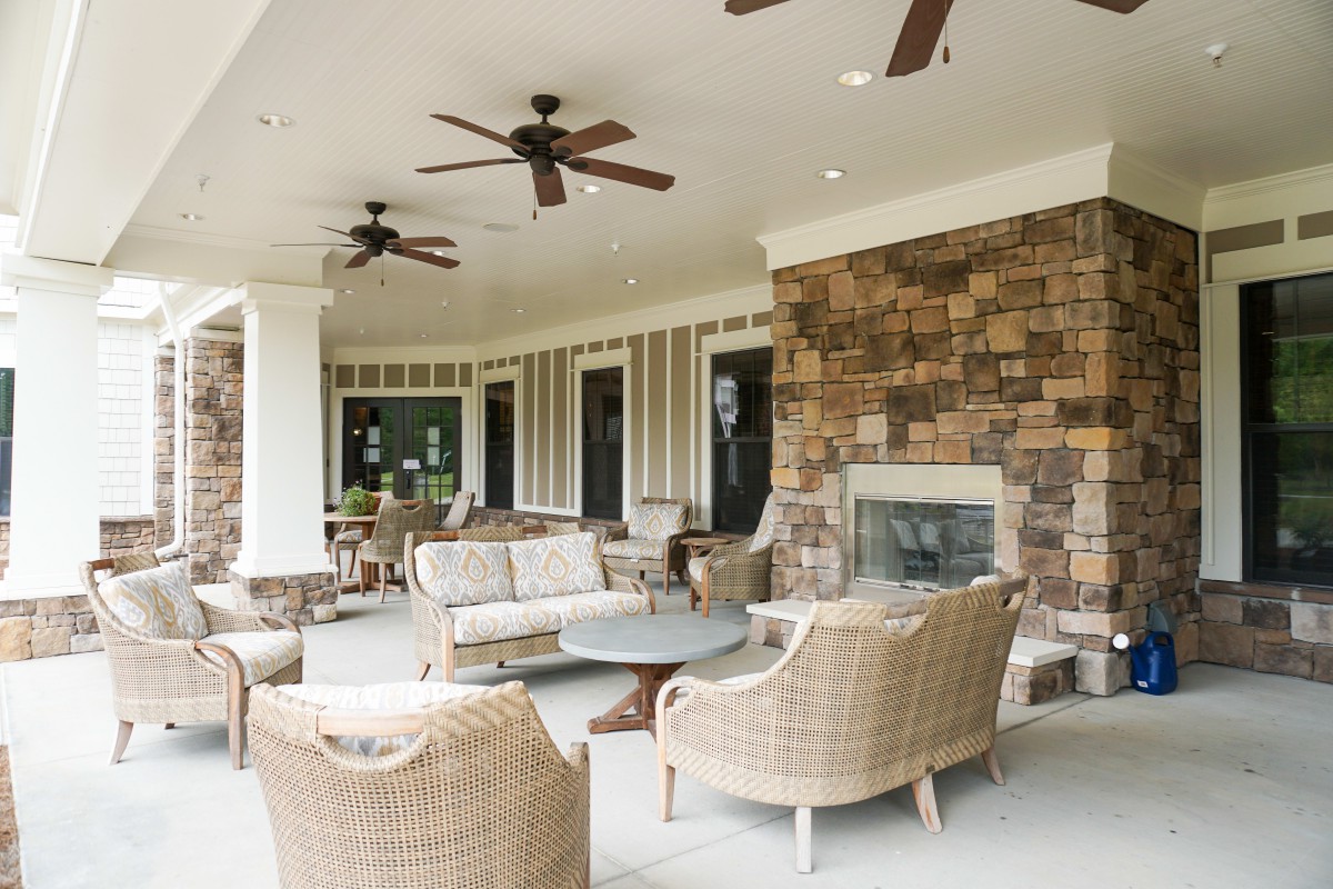 A cozy outdoor patio with wicker furniture, ceiling fans, and a stone fireplace.