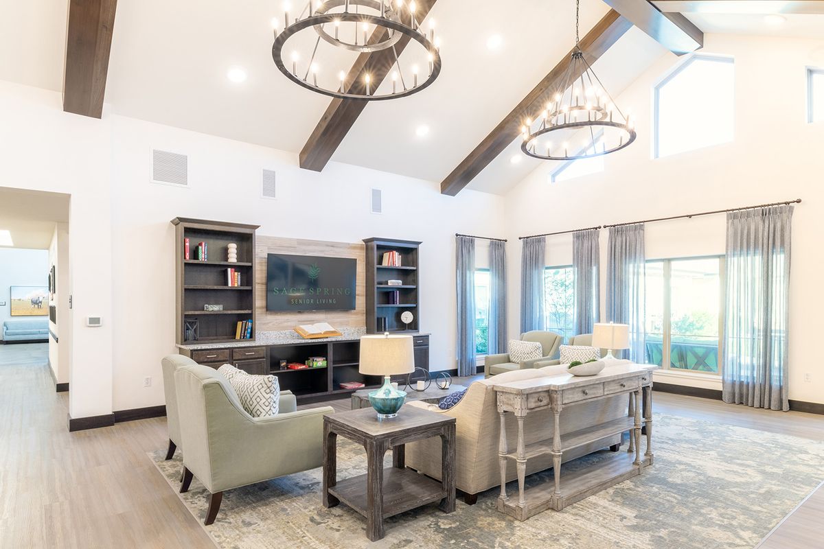 A spacious and modern living room featuring elegant chandeliers, comfortable sofas, and a stylish bookshelf.
