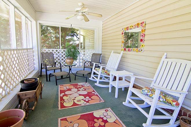 A cozy porch featuring rocking chairs, colorful rugs, and a ceiling fan, perfect for relaxing outdoors.