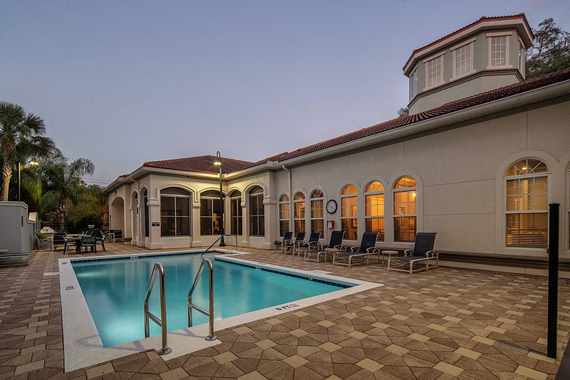 An outdoor swimming pool beside a well-lit building in the evening.