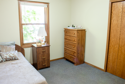A cozy, minimalist bedroom featuring a wooden dresser and bedside table with a lamp.
