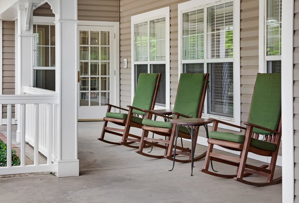 A cozy porch with green-cushioned rocking chairs lined up neatly.