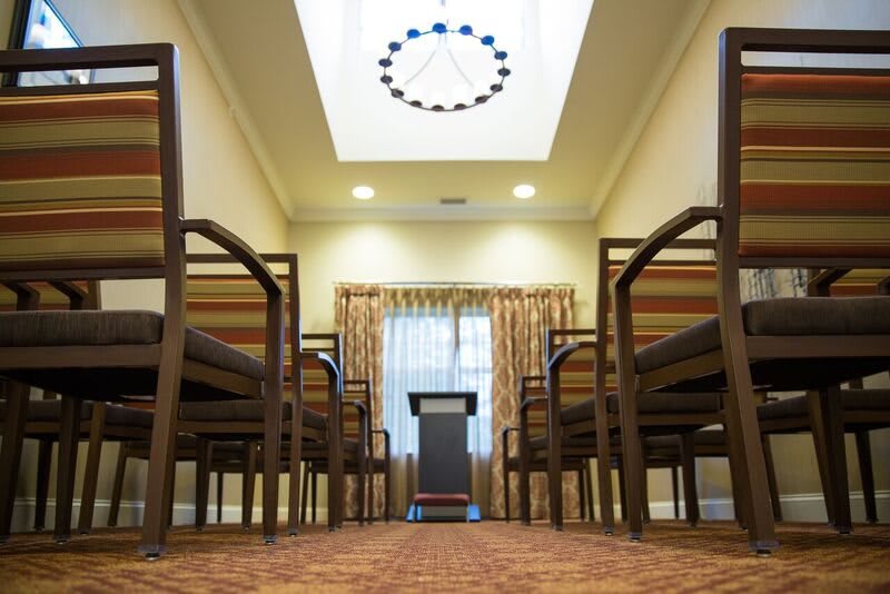 An interior view of a room with chairs arranged facing a podium, featuring a carpeted floor and overhead lighting.