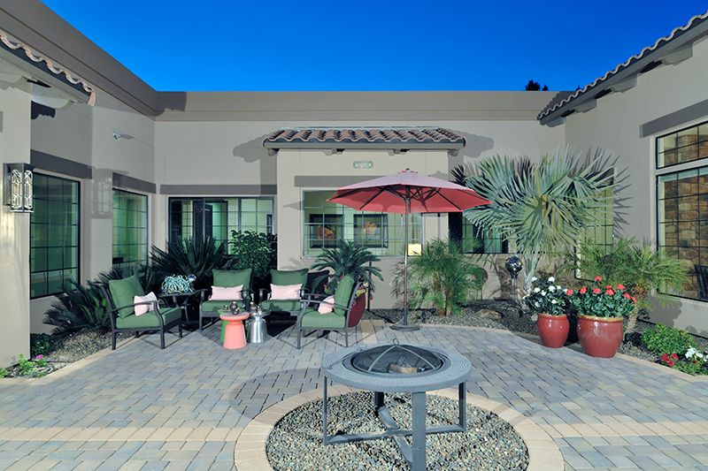 A cozy patio setup featuring outdoor furniture, a red umbrella, a fire pit, and lush plants in an evening setting.
