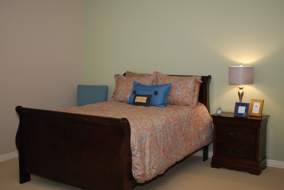A cozy bedroom with a neatly made bed and a nightstand featuring a lamp.