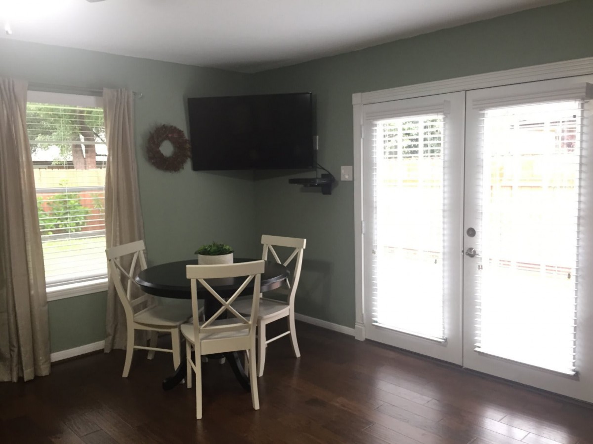 A cozy dining nook with a round table and chairs, featuring a wall-mounted television and bright French doors.