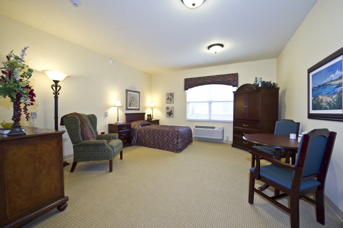 A spacious bedroom with a single bed, armchair, and wooden furniture.
